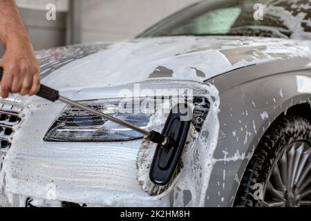 Lumière avant de silver car lavés dans le libre service carwash, man hand holding pinceau, nettoyage de la vitre avec du shampoing Banque D'Images