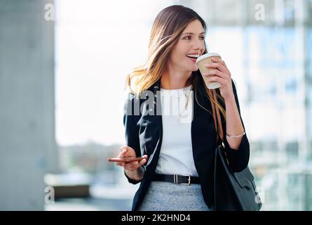 Commencez votre journée avec de la caféine. Photo courte d'une jeune femme d'affaires qui boit du café tout en marchant dans un bureau moderne. Banque D'Images