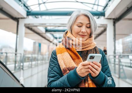 Une femme âgée envoie un message avec un téléphone mobile dans une station de transport Banque D'Images