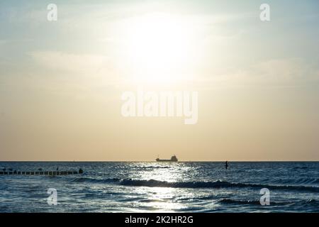 Coucher de soleil sur la mer, un navire à l'horizon, avec des groynes et des goélands Banque D'Images