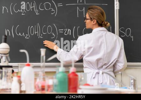Professeur expliquant comment lire une équation chimique sur un tableau de surveillance pendant une leçon de chimie Banque D'Images