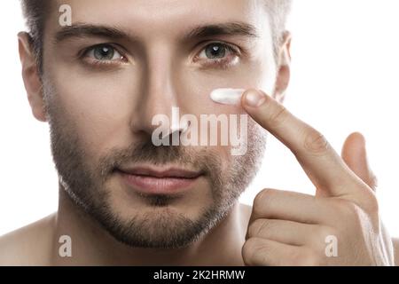 La beauté des hommes. Le jeune homme applique de la crème hydratante et anti-âge sur son visage Banque D'Images