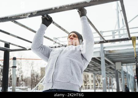 Homme sportif qui fait des pull-ups sur la barre horizontale pendant son entraînement d'hiver en plein air Banque D'Images