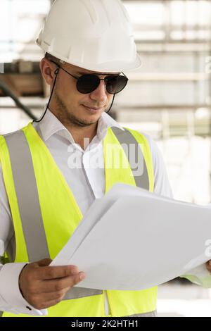 Homme architecte portant un gilet de sécurité avec des plans sur un chantier de construction Banque D'Images