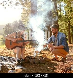 Chansons de feu de camp.Prise de vue d'une jeune femme jouant de la guitare pour son petit ami à leur campement. Banque D'Images