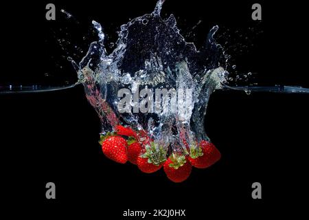 Bouquet de fraises fraîches mûres tombées dans l'eau avec des éclaboussures isolées sur fond noir. Banque D'Images