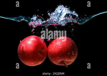 Gros plan de deux pommes rouges jetées sous l'eau avec des éclaboussures sur le noir. Banque D'Images