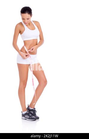 Elle est un fanatique de santé.Photo en studio d'une jeune femme en forme de femme qui prend ses mesures isolées sur blanc. Banque D'Images