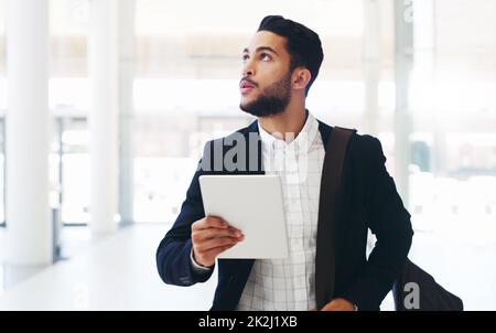 Soyez toujours attentif à la prochaine opportunité.Photo courte d'un jeune homme d'affaires charmant utilisant une tablette tout en marchant dans le bureau pendant la journée. Banque D'Images