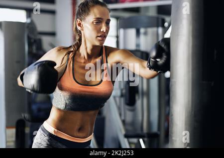 Le sortir sur le sac.Coupe courte d'un boxeur féminin s'entraîner sur un sac de poinçonnage dans la salle de sport. Banque D'Images