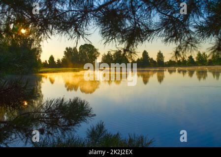 Brume matinale au-dessus d'un lac tranquille au lever du soleil Banque D'Images