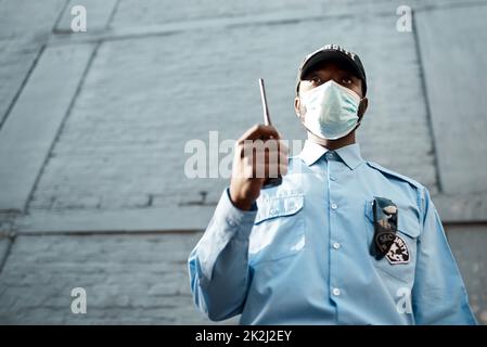 Protection proactive pour la protection de vos propriétés. Photo d'un jeune agent de sécurité masqué à l'aide d'une radio bidirectionnelle lors d'une patrouille à l'extérieur. Banque D'Images