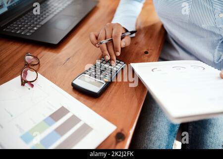 Les affaires sont un jeu de chiffres. Photo rognée d'une femme d'affaires utilisant une calculatrice tout en passant par les documents financiers à son bureau. Banque D'Images