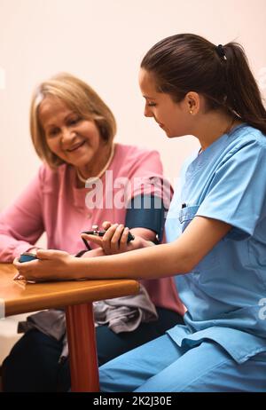 Il semble que votre tension artérielle ait bien diminué. Injection de sang d'une infirmière qui vérifie la tension artérielle d'un patient âgé. Banque D'Images