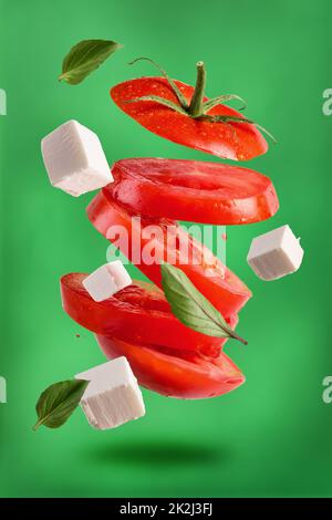 Une cuisine végétarienne saine et savoureuse. Tomates juteuses mûres coupées avec fromage doux et feuilles de basilic frais sur fond vert Banque D'Images