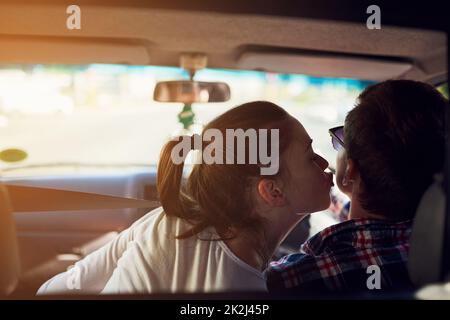 Certains baisers ne peuvent pas attendre. Vue arrière d'une jeune femme embrassant son petit ami pendant qu'il conduit une voiture. Banque D'Images