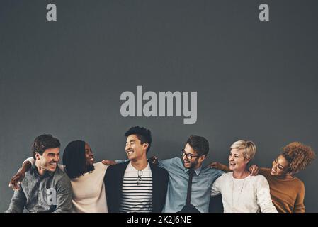 Nous faisons une excellente équipe.Photo en studio d'un groupe diversifié d'employés créatifs s'embrassant les uns les autres sur un fond gris. Banque D'Images