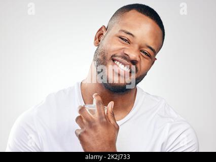 Ce parfum vient compléter mon style personnel. Studio portrait d'un beau jeune homme vaporisant du parfum sur lui-même sur un fond blanc. Banque D'Images