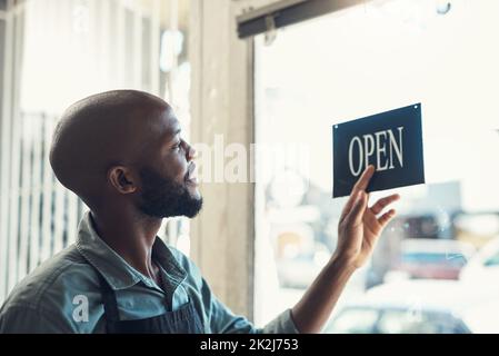 Tourner l'affiche est ma partie préférée de la journée. Photo d'un beau jeune homme debout et tournant le panneau sur la porte de son magasin de vélos. Banque D'Images