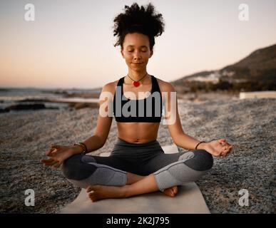 Zen ultime. Prise de vue en longueur d'une jeune femme attrayante pratiquant le yoga sur la plage au coucher du soleil. Banque D'Images