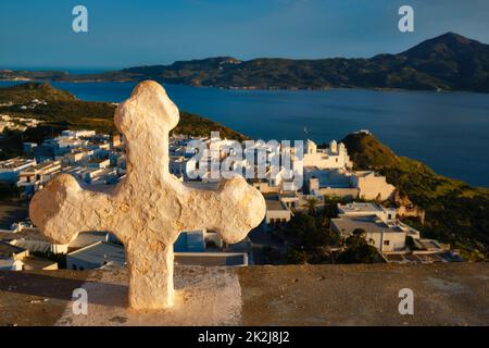 Croix chrétienne et village de Plaka sur l'île de Milos sur rouge Géranium fleurs au coucher du soleil en Grèce Banque D'Images