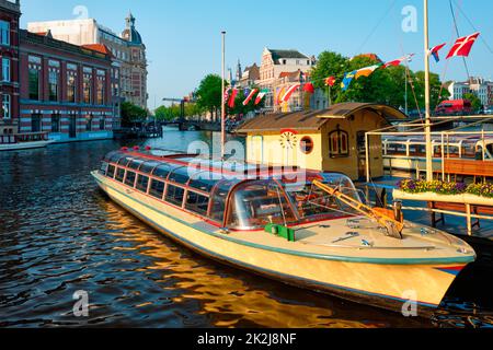 Bateaux touristiques amarrés sur le quai du canal d'Amsterdam au coucher du soleil Banque D'Images