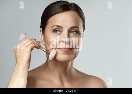 Belle femme d'âge moyen utilisant un rouleau de quartz rose Banque D'Images