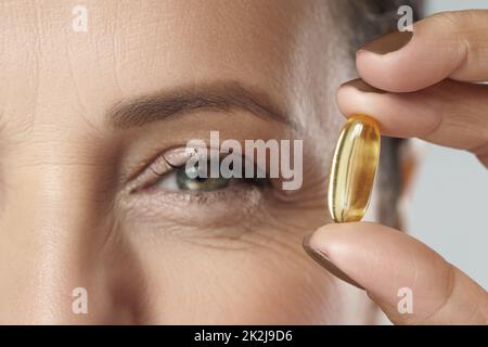 Femme d'âge moyen tenant une capsule avec une source de poisson ou d'huile de krill d'acides gras oméga-3 Banque D'Images