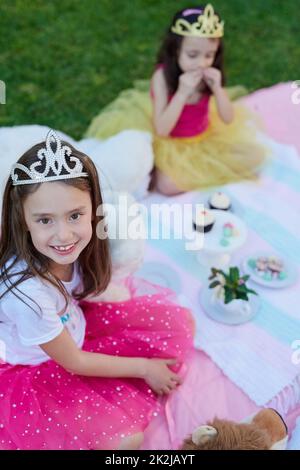 Même les princesses aiment les pique-niques. Portrait d'une petite fille ayant un pique-nique avec sa sœur à l'extérieur. Banque D'Images