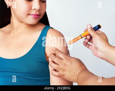 Mais tout d'abord, l'insuline. Photo studio d'une jeune fille mignonne recevant une injection d'insuline d'une femme méconnaissable sur fond gris. Banque D'Images