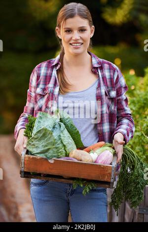 Uniquement biologique. Portrait d'une jeune femme heureuse tenant une caisse pleine de légumes fraîchement cueillis. Banque D'Images