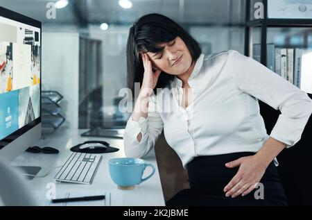 Pourquoi cela fait-il tant de mal. Plan court d'une femme d'affaires enceinte attrayante assise seule dans le bureau et souffrant de douleurs abdominales. Banque D'Images