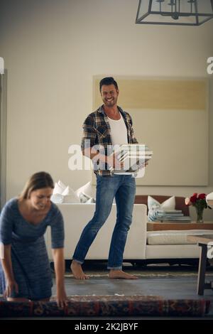 Avez-vous besoin d'aide ? Photo d'une jeune belle femme roulant sur un tapis tandis que son beau mari porte des livres à la maison. Banque D'Images