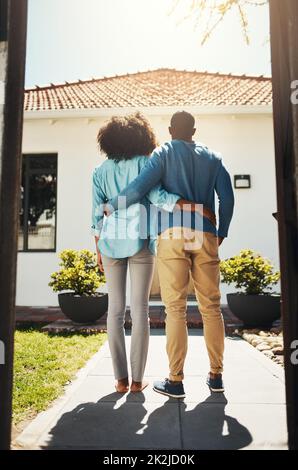 Découvrez notre nouvel endroit. Vue arrière d'un couple méconnaissable se tenant debout et regardant sa nouvelle maison. Banque D'Images