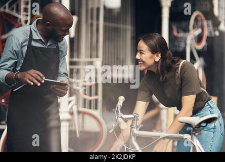 Nos vélos vintage sont les plus populaires. Photo d'un beau jeune homme debout à l'extérieur de son magasin de vélos et aidant un client. Banque D'Images