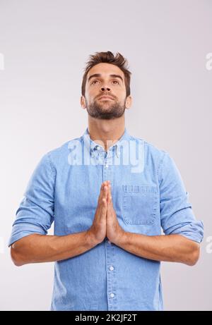 Dieu, s'il vous plaît, répondez-moi. Studio photo d'un beau jeune homme priant sur fond gris. Banque D'Images