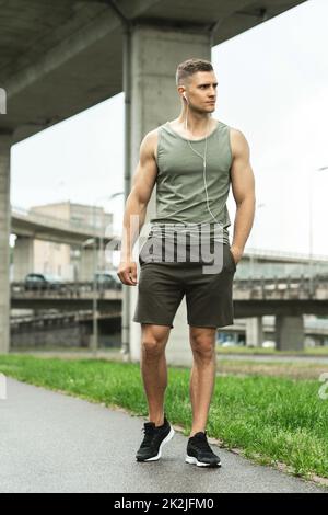 Homme beau avec des écouteurs. Écouter de la musique pendant un entraînement physique dans la rue. Banque D'Images