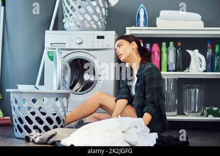 Je préfère faire QUOI que ce soit d'autre en ce moment Prise de vue d'une jeune femme attrayante qui a l'air de s'ennuyer tout en faisant le linge à la maison. Banque D'Images