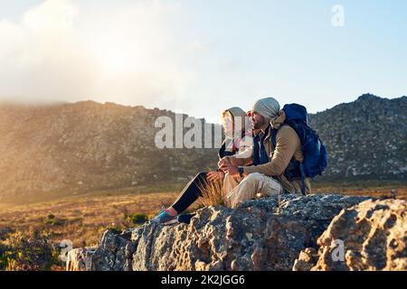 La meilleure vue vient de la montée la plus difficile. Photo de deux randonneurs assis au sommet d'une montagne ayant une conversation. Banque D'Images