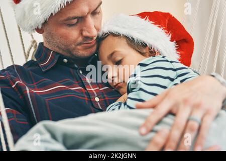 L'endroit le plus sûr dans le monde entier. Photo d'un adorable petit garçon ayant une sieste avec son père dans un hamac à Noël. Banque D'Images