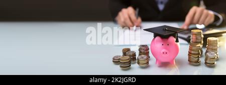 Close-up of Piggy Bank Wearing Graduation Hat et pièces empilées Banque D'Images