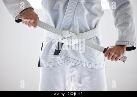 Prêt à démarrer. Coupe courte d'un artiste martial masculin méconnu qui attache sa ceinture à la salle de sport. Banque D'Images