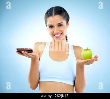 La santé est un choix. Studio de photo d'une femme qui décide entre des aliments sains et malsains. Banque D'Images