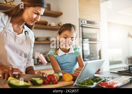 Ils aiment essayer de nouvelles choses. Photo d'une mère et de sa jeune fille essayant ensemble une nouvelle recette dans la cuisine. Banque D'Images