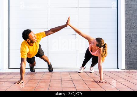 Entraînement de couple sportif interracial à l'extérieur - couple multiracial portant des vêtements de sport et faisant de l'entraînement fonctionnel à l'extérieur pour les muscles tendus du corps, Banque D'Images