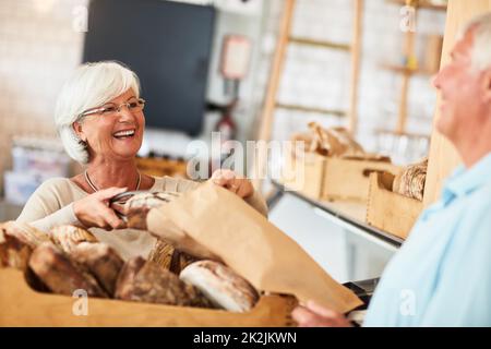 J'espère que vous l'apprécierez parce que j'ai apprécié la cuisson. Photo d'une femme âgée heureuse servant un client dans une boulangerie. Banque D'Images