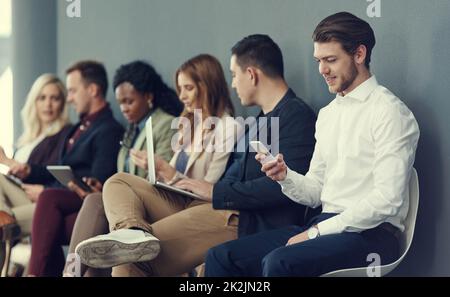 La file d'attente de réussite. Photo d'un groupe d'hommes d'affaires utilisant différents appareils sans fil en attendant une interview. Banque D'Images