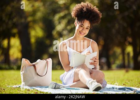 C'est mon endroit préféré pour le journal. Portrait en longueur d'une jeune femme attrayante écrivant dans son journal tout en étant assise dans le parc. Banque D'Images