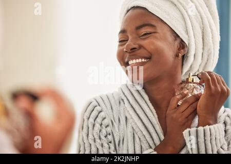 C'est mon parfum préféré. Photo d'une jeune femme qui a l'air gaie tout en utilisant du parfum. Banque D'Images