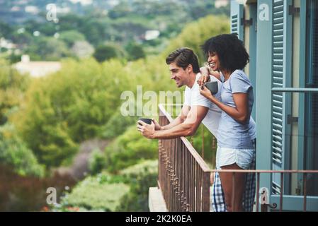 Cet endroit est tout simplement incroyable. Photo d'un jeune couple affectueux qui boit un café et qui regarde la vue tout en se tenant sur un balcon à la maison. Banque D'Images